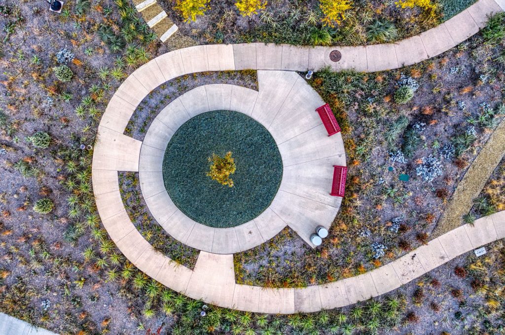 Projeto brasileiro transforma área hospitalar em jardim terapêutico e vence prêmio em Milão Vista aérea de jardim paisagístico com caminho circular entre áreas verdes.