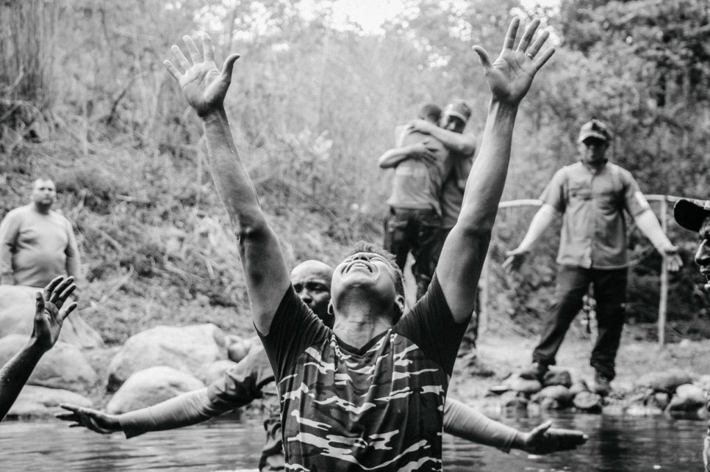Grupo de homens participa de um batismo cristão nas águas de um rio.